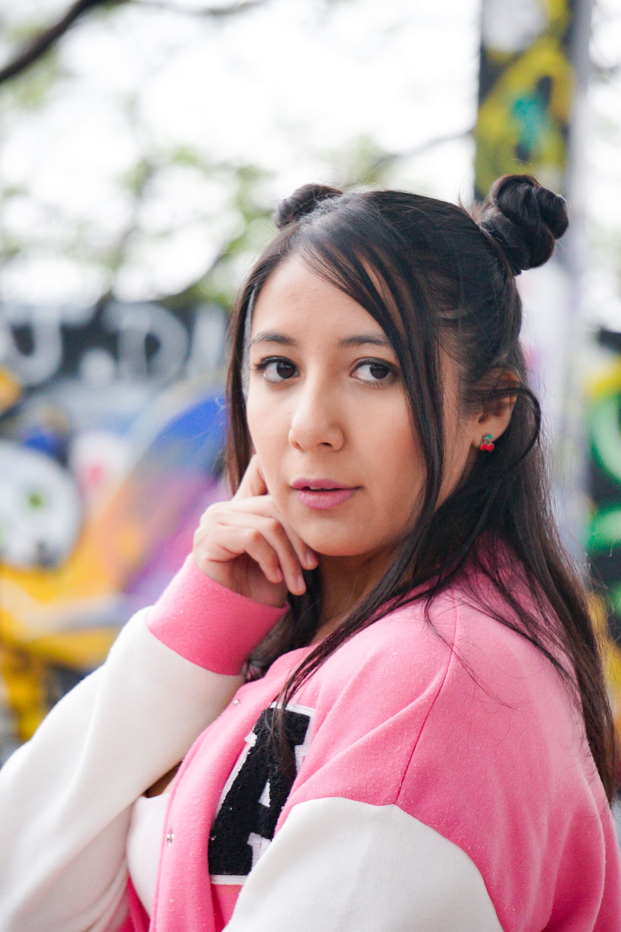 Confident woman in a vibrant pink jacket poses against colorful graffiti in Mexico City's urban landscape.