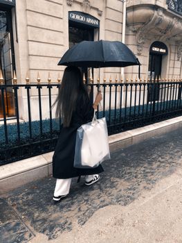 A woman with an umbrella walks along Avenue Montaigne in Paris near Giorgio Armani during a rainy day.
