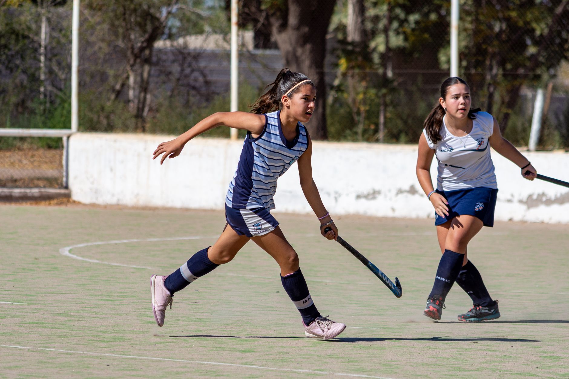 Girls playing an intense game of field hockey on an outdoor court during the day.