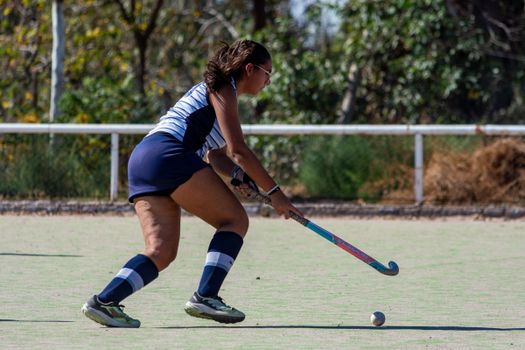 A female field hockey player focused on the ball during a game on an outdoor field.