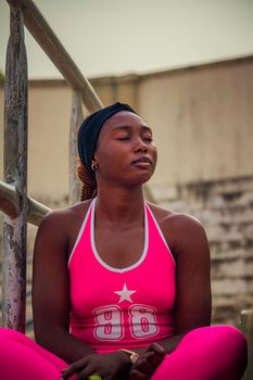 A young adult woman in pink athletic wear meditates outdoors, exuding calm and focus.