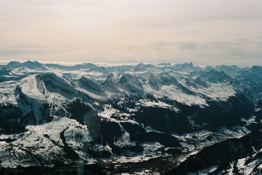 Spectacular aerial view of snow-covered Alpine mountain range under a serene sky.