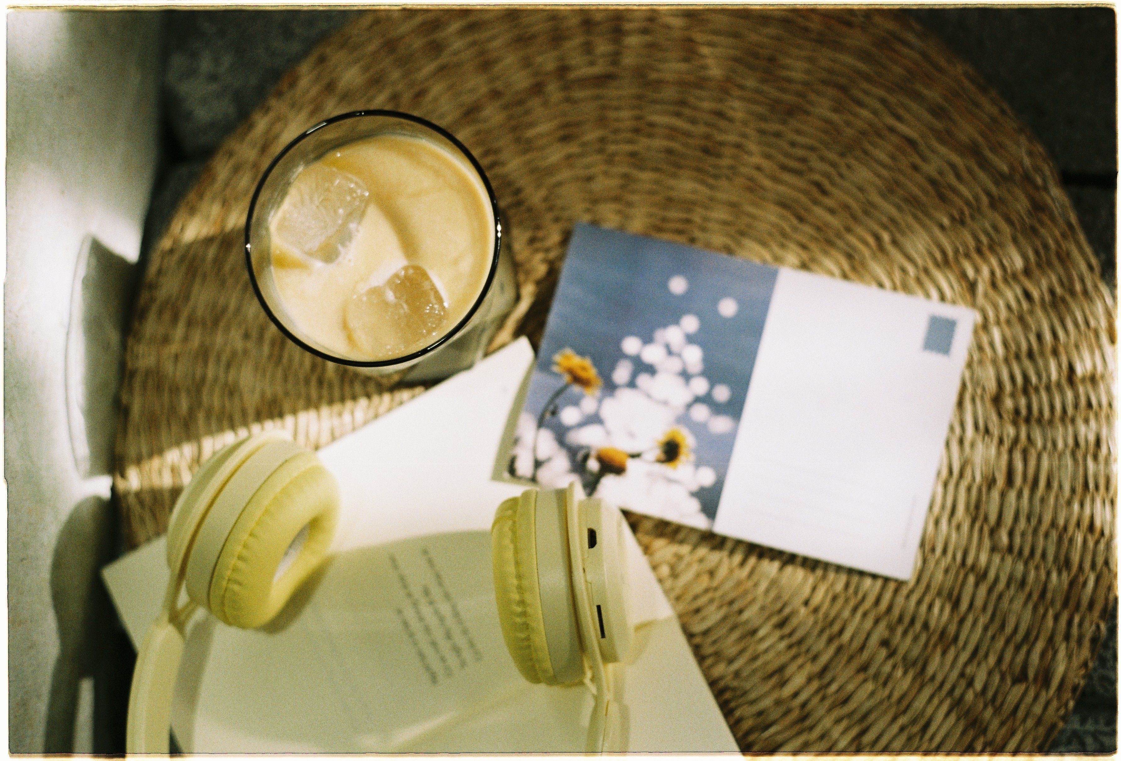 Relaxing scene with iced coffee, headphones, and postcard.