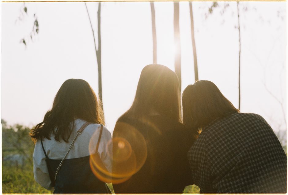 Three friends share a moment outdoors, bathed in warm, backlit sunlight.