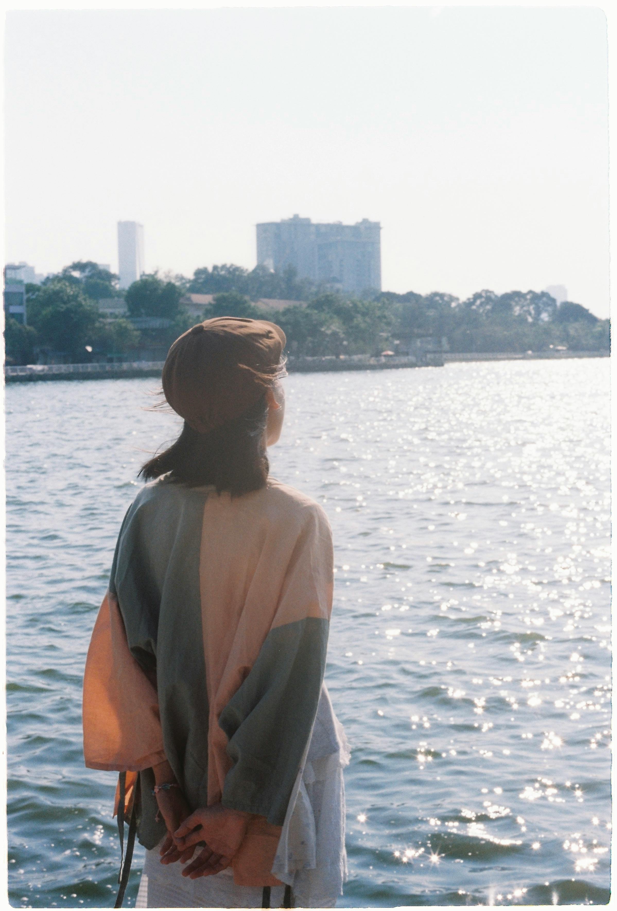 A woman in a beret looks over the city skyline from a waterfront view.