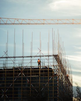 Scaffold workers in safety gear working on a building at sunset with clear sky.