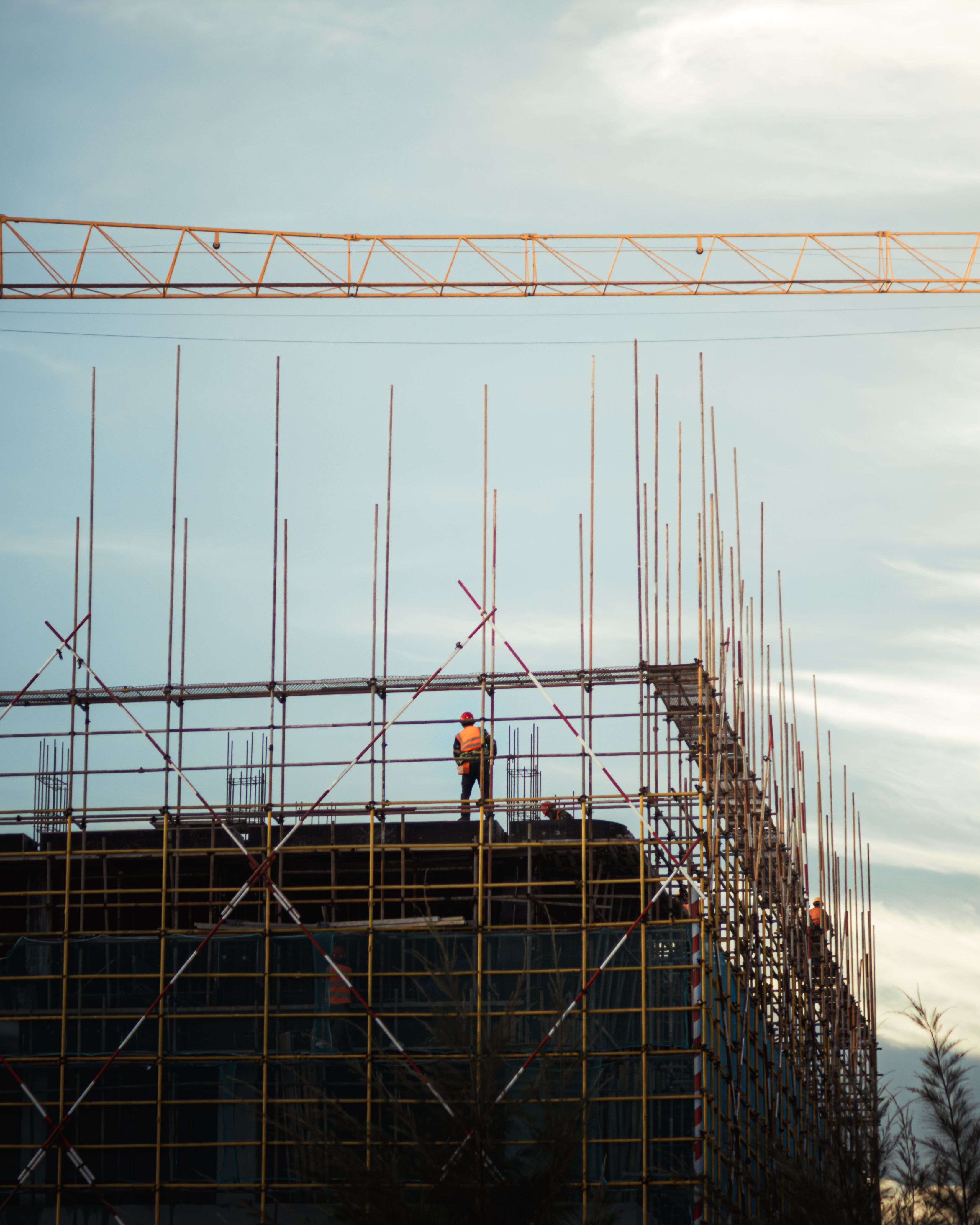 QBCC Licence Renewal: Deadlines, Fees and What Happens If You Miss It 1 Construction site at sunset with workers on scaffolding and a crane