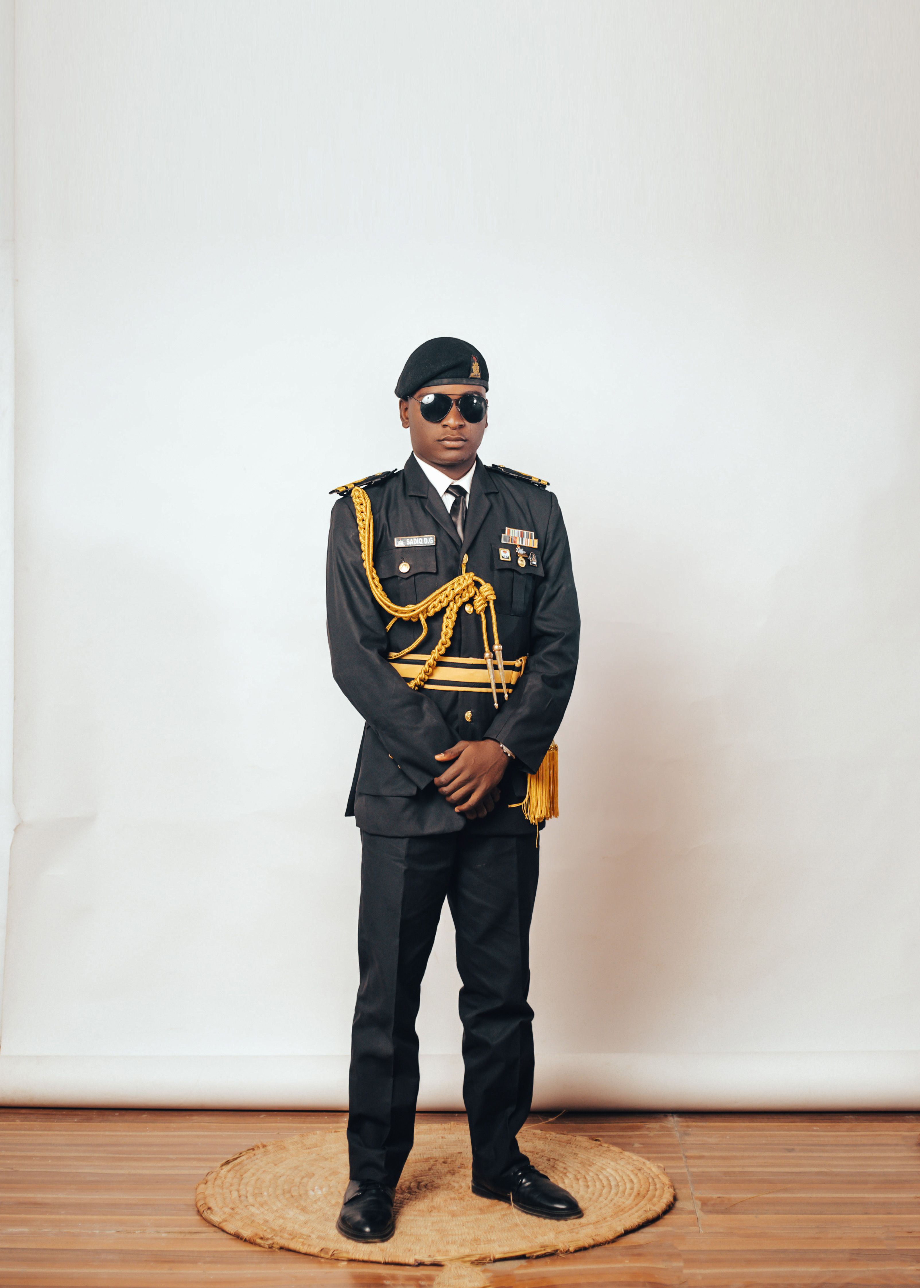 A stylish portrait of a young man in full military uniform indoors with a neutral background.