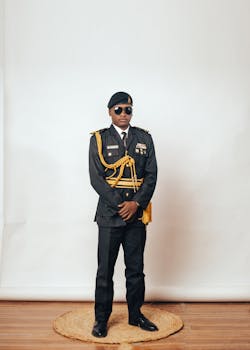 A stylish portrait of a young man in full military uniform indoors with a neutral background.