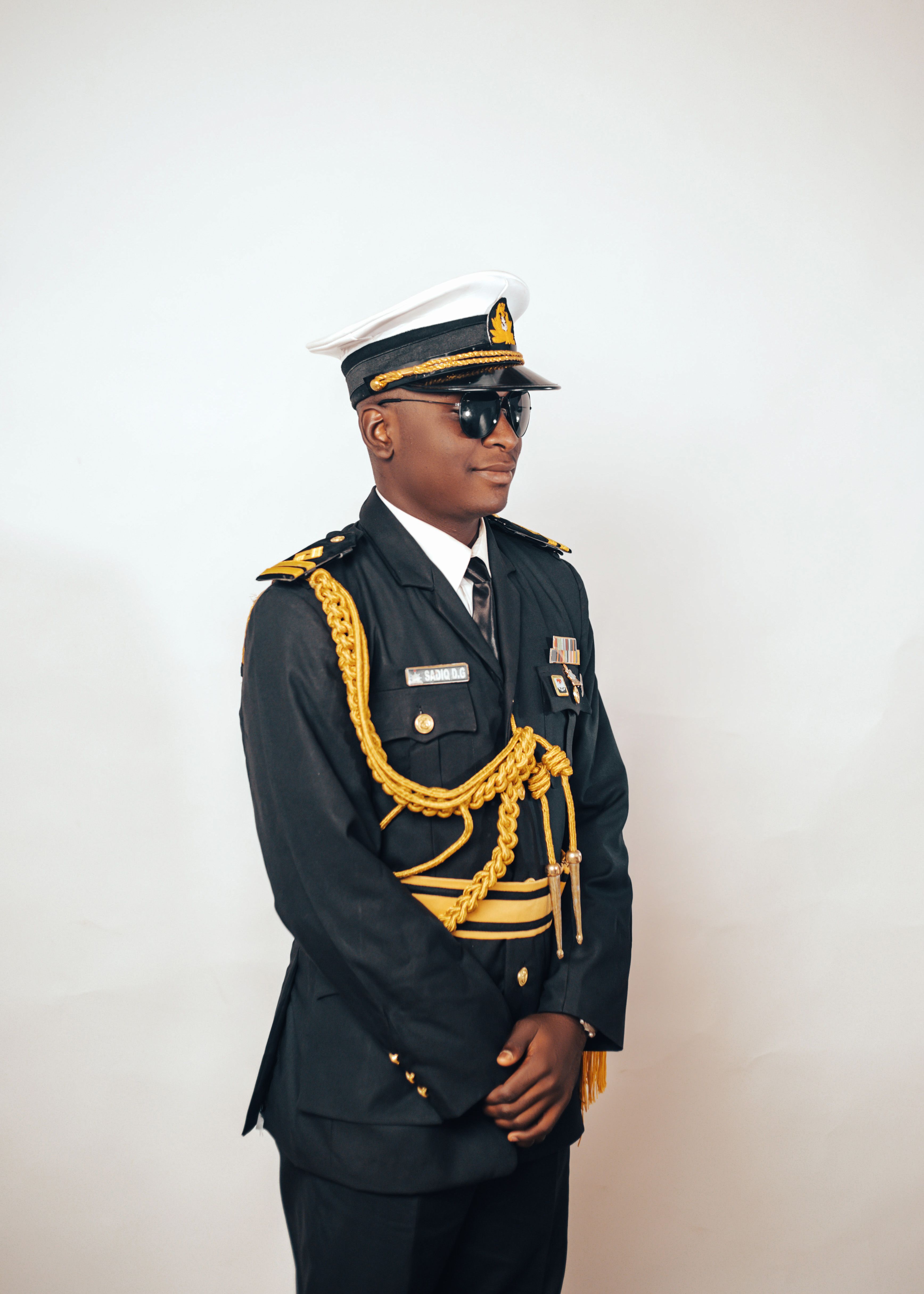 A young naval officer in full dress uniform with medals, posing confidently indoors.