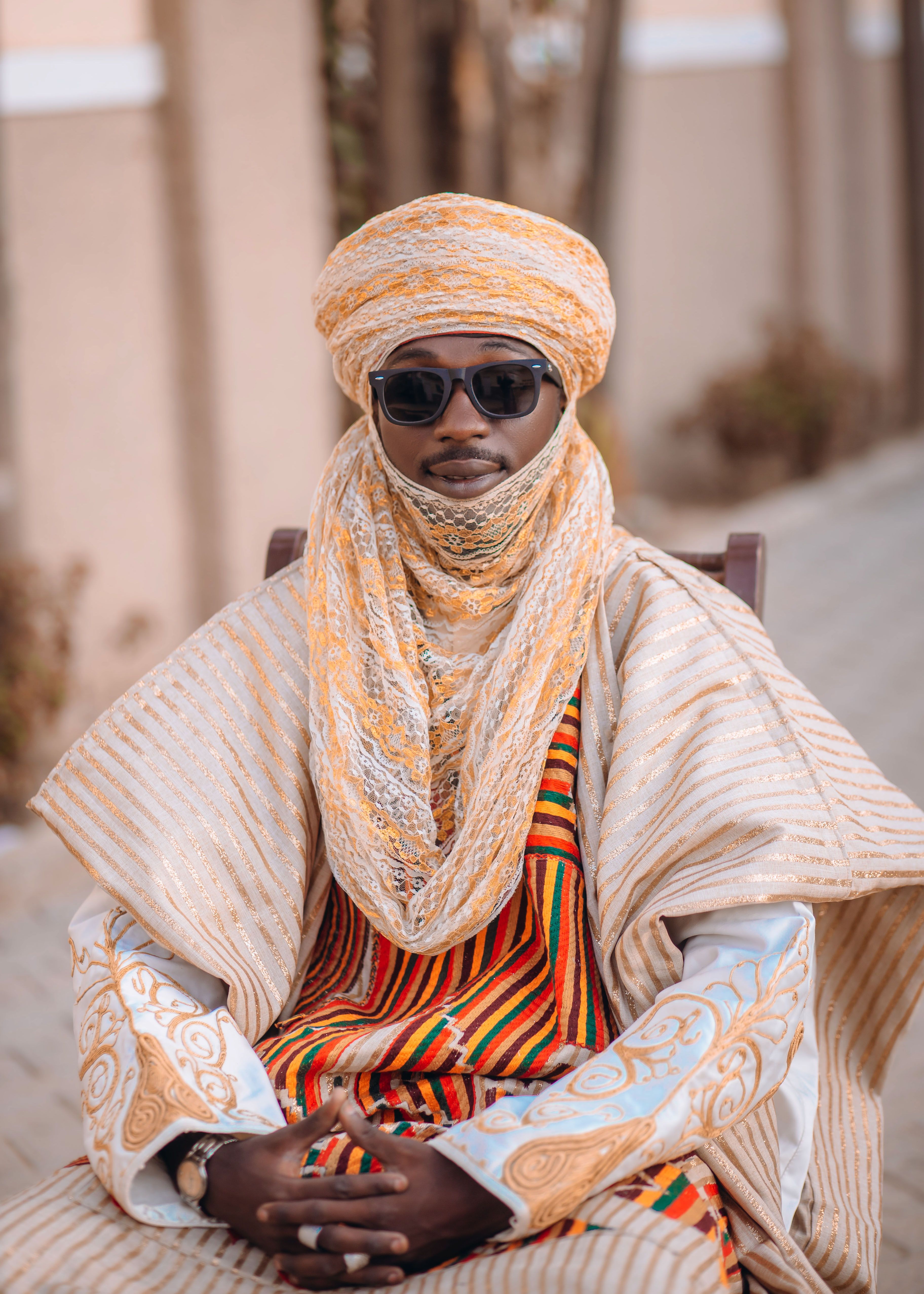 An adult man wearing traditional African attire and sunglasses, sitting outdoors.