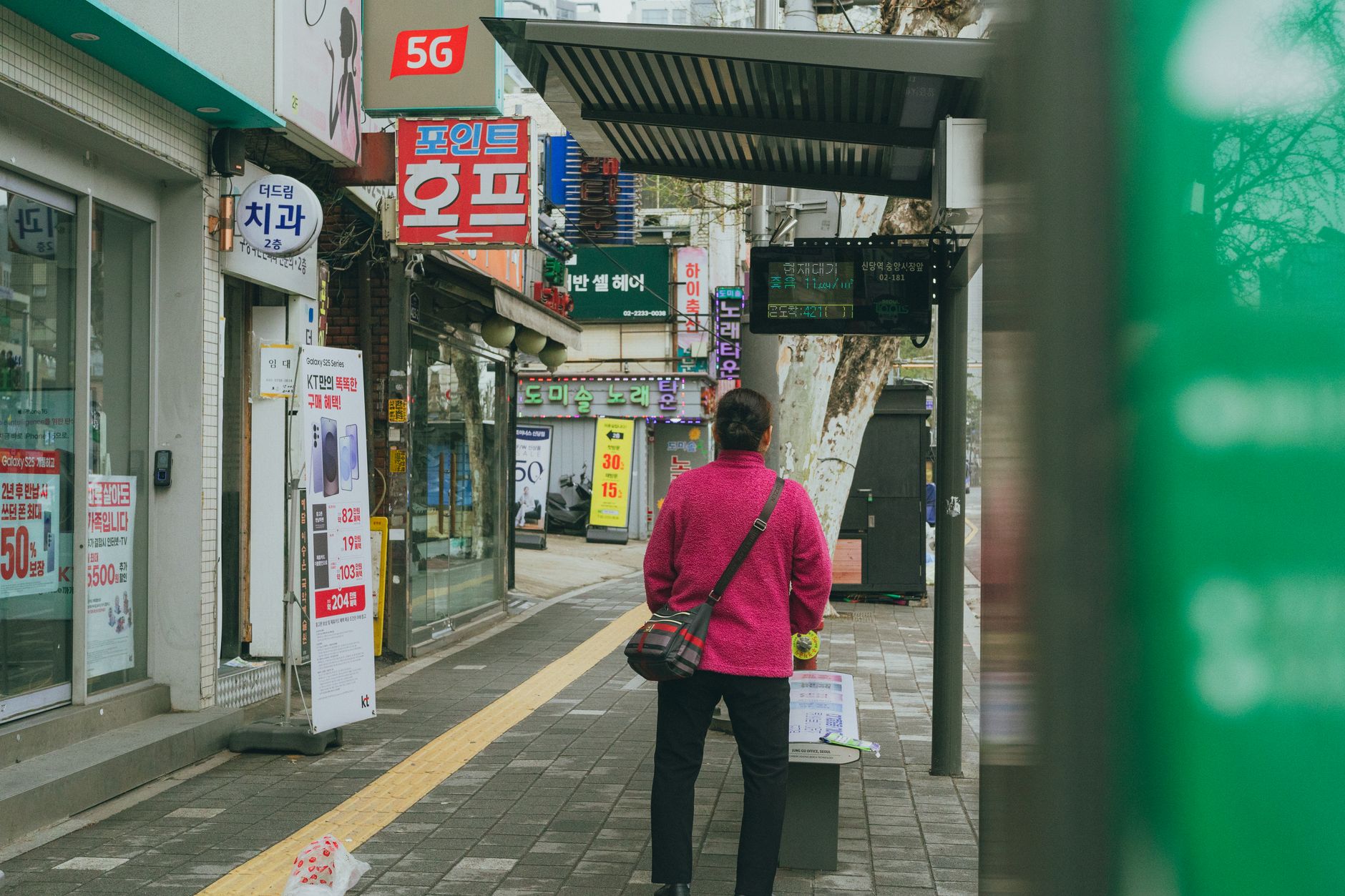 A person waits at a bus stop in Seoul, South Korea, featuring vibrant street signage.