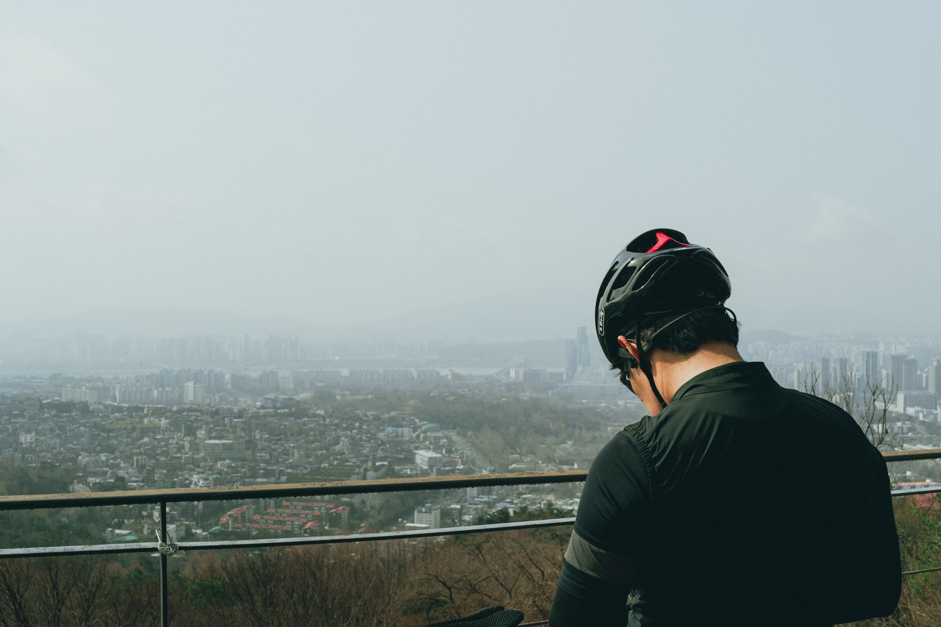 A cyclist wearing a helmet looks over the Seoul skyline, capturing the merging of urban life and natural serenity.