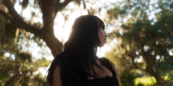 Backlit portrait of a woman in a serene forest setting with sunlight filtering through the trees.