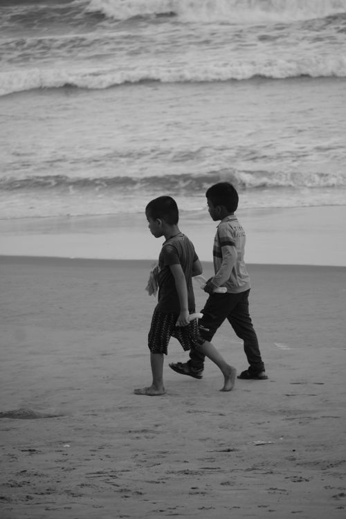Free Two children walking along a beach shore captured in black and white, evoking a nostalgic and serene mood. Stock Photo