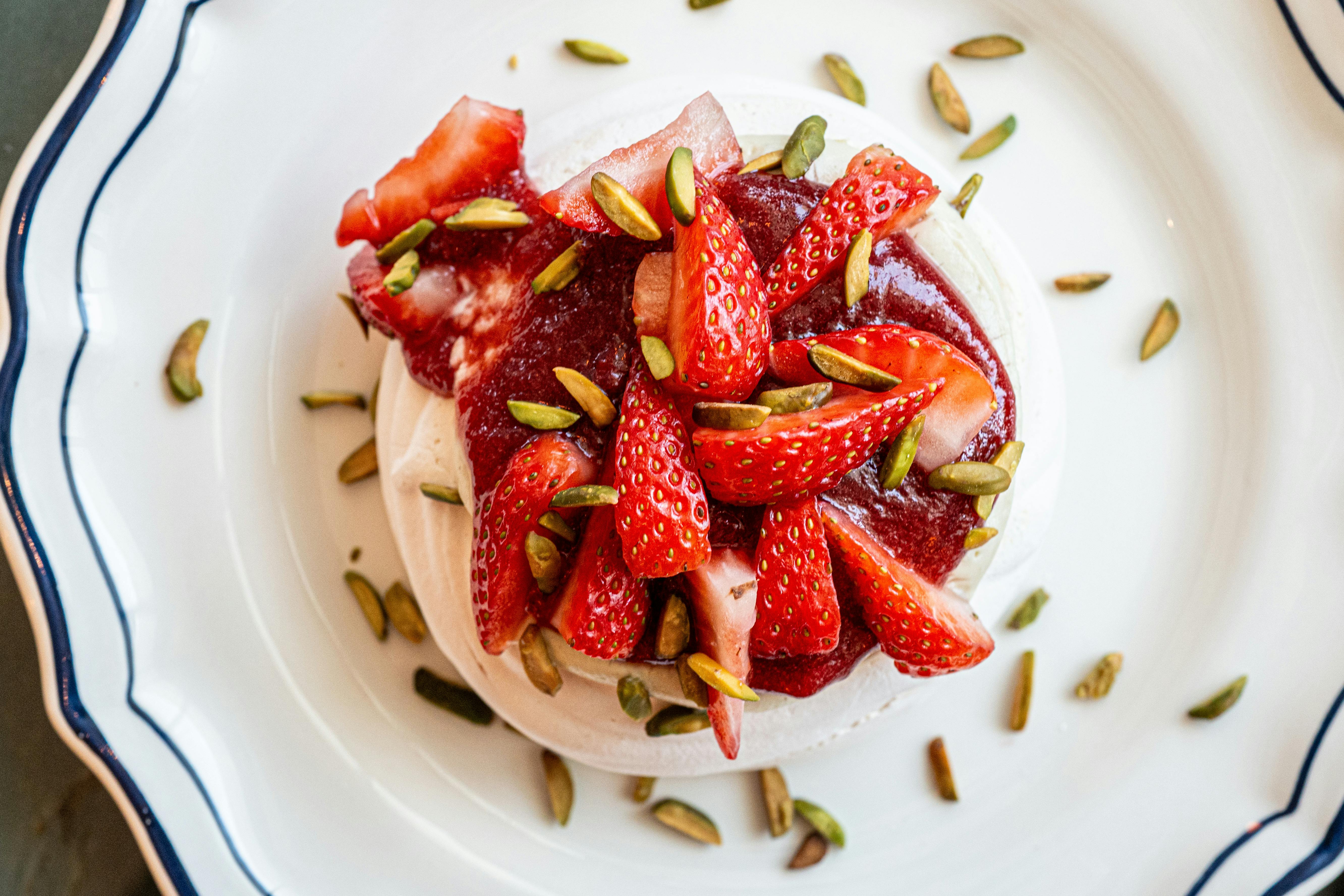 Top view of gourmet strawberry dessert with pistachios on elegant plate.