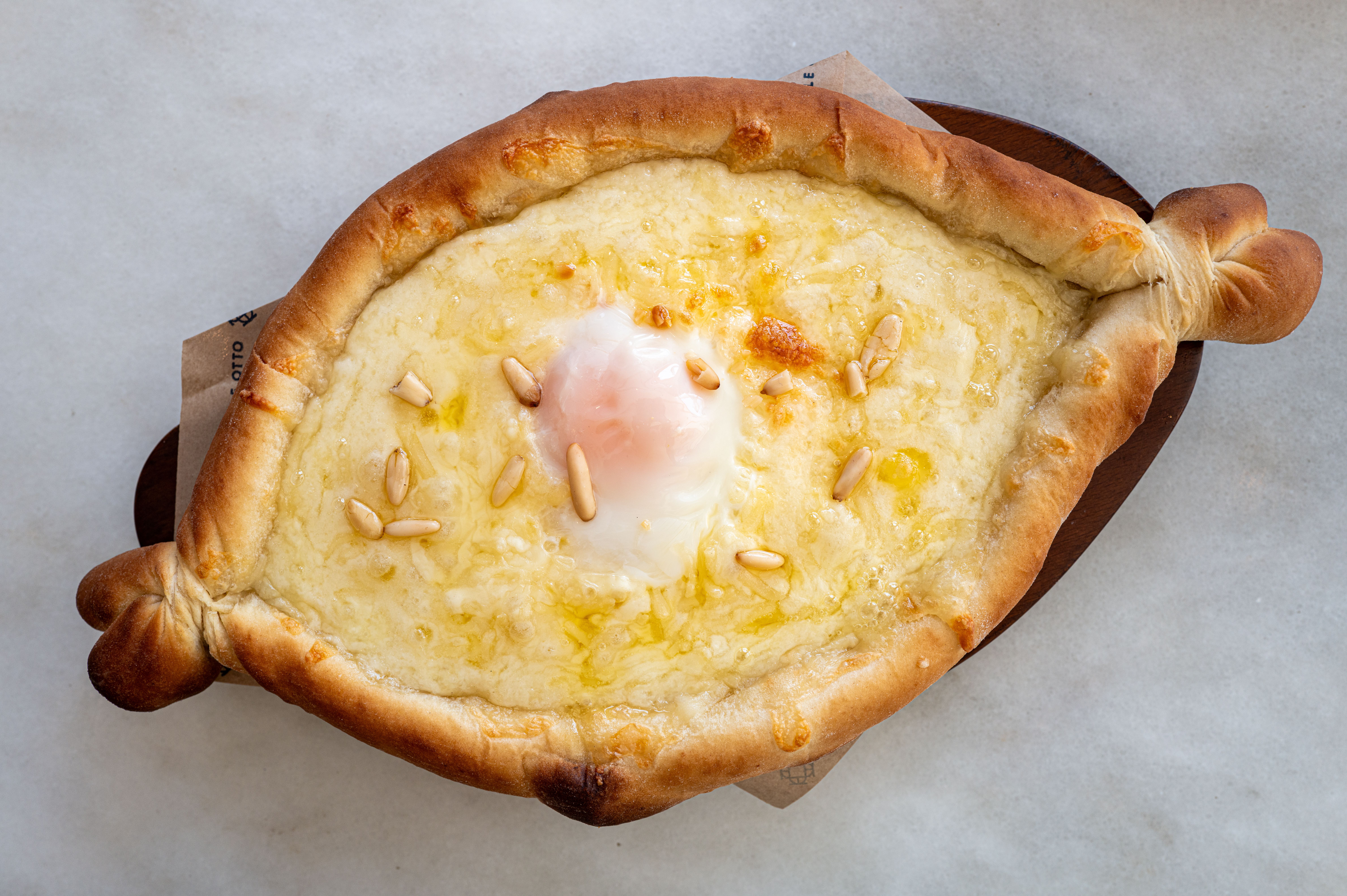 Traditional Georgian Khachapuri topped with cheese, egg, and pine nuts on a marble surface.