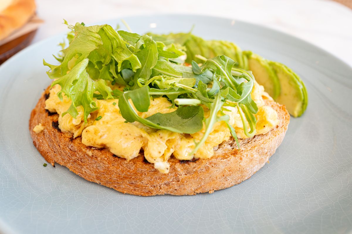 Creamy scrambled eggs on a thick toast round topped with arugula and avocado slices