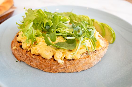 Creamy scrambled eggs on a thick toast round topped with arugula and avocado slices