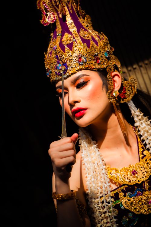 Free Elegant Balinese dancer in vibrant traditional attire and golden headdress performing under dramatic lighting. Stock Photo
