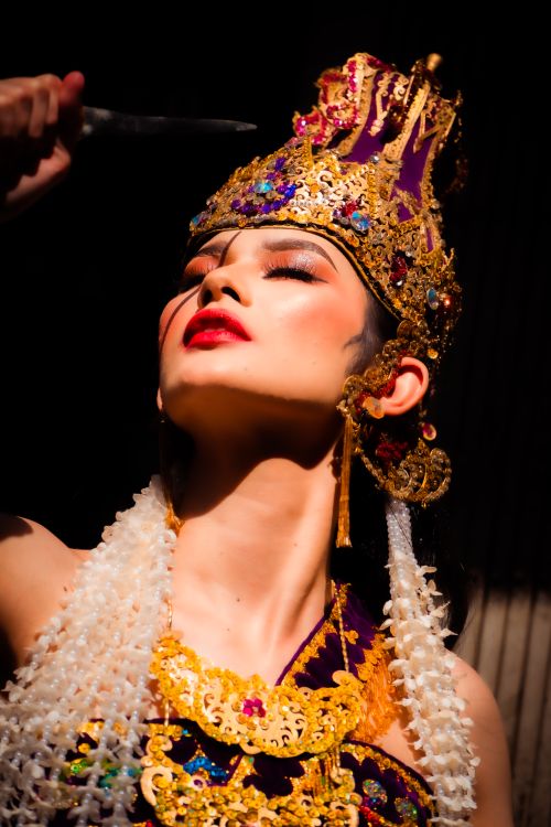 Free Striking portrait of woman in colorful Balinese attire with ornate headdress under dramatic lighting. Stock Photo