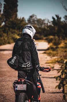 A motorcyclist in protective gear rides down a deserted country road, surrounded by fall foliage.