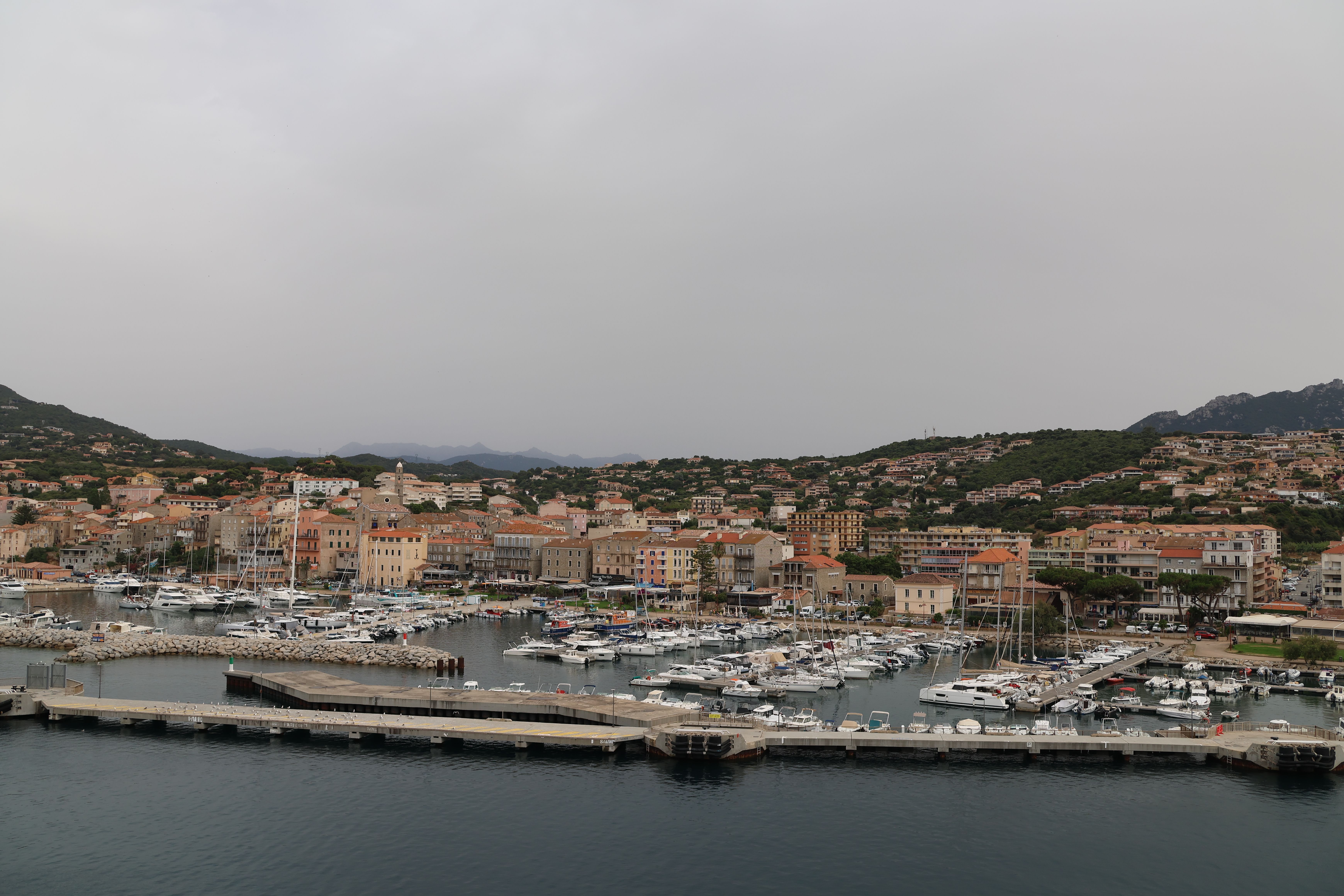 Scenic view of a harbor town with yachts moored at the marina, set against lush hills.