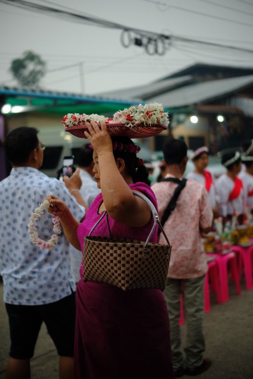 Free A woman carries a tray of flowers on her head in a vibrant street market scene. Stock Photo