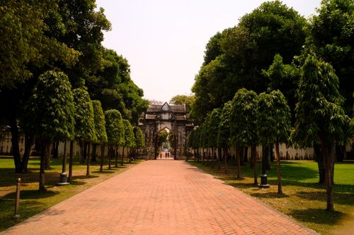 Free Beautiful park pathway with green trees leading to a historic stone arch in a sunny outdoor setting. Stock Photo