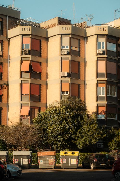 Free A city apartment building with trees and trash bins in the foreground on a sunny day. Stock Photo