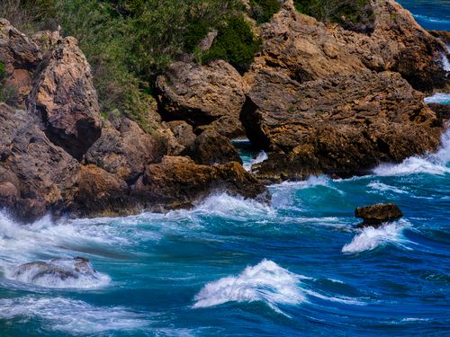 Free Stunning view of a rocky coastline with turbulent waves and clear blue waters. Stock Photo