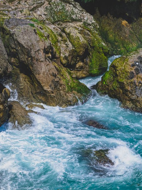 Free Vivid blue waves crashing against mossy rocks, creating a dramatic seascape scene. Stock Photo