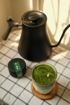 Stylish matcha latte with modern kettle on checkered tablecloth. Perfect zen refreshment.