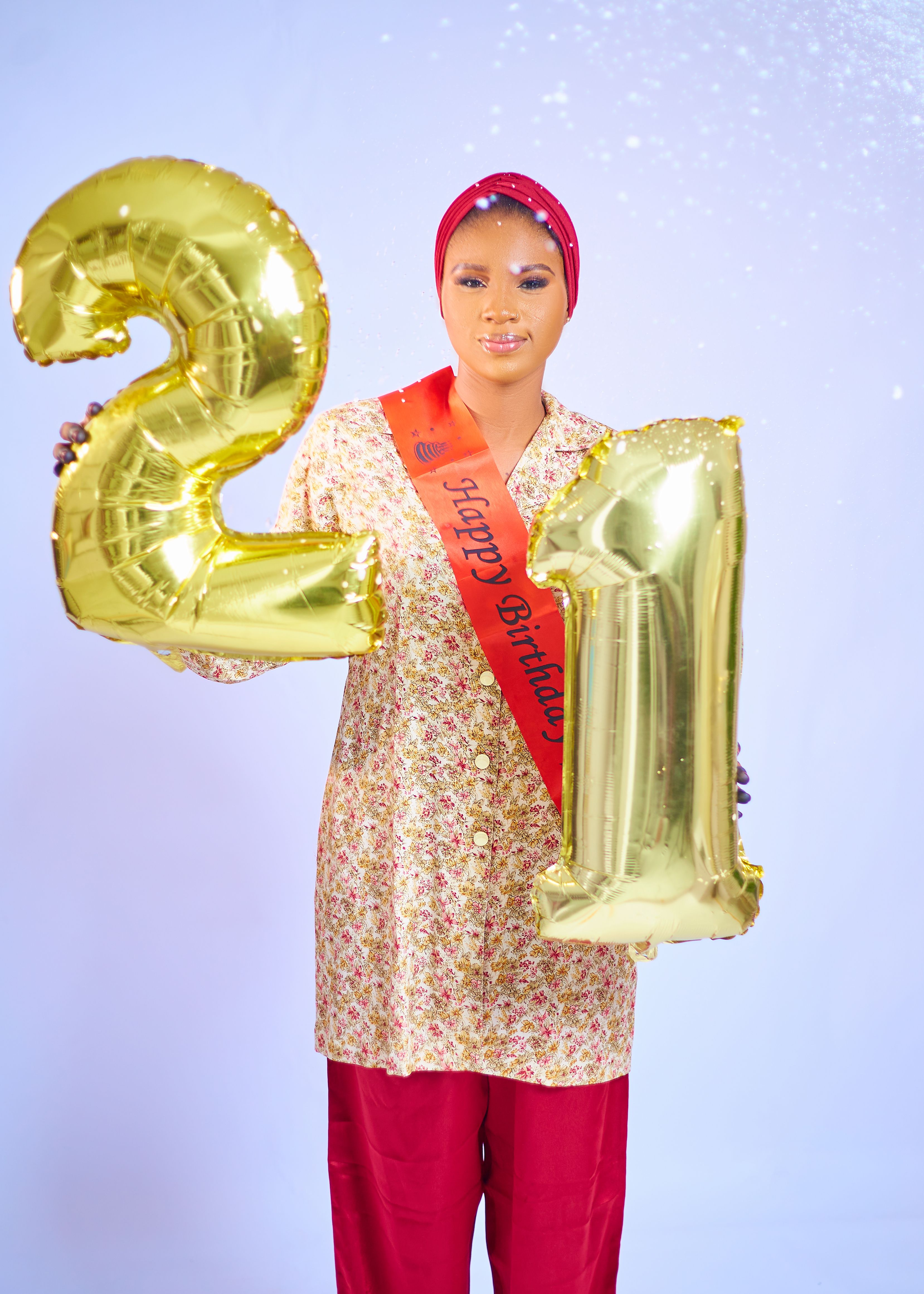 A woman in festive attire celebrates her 21st birthday with gold number balloons.