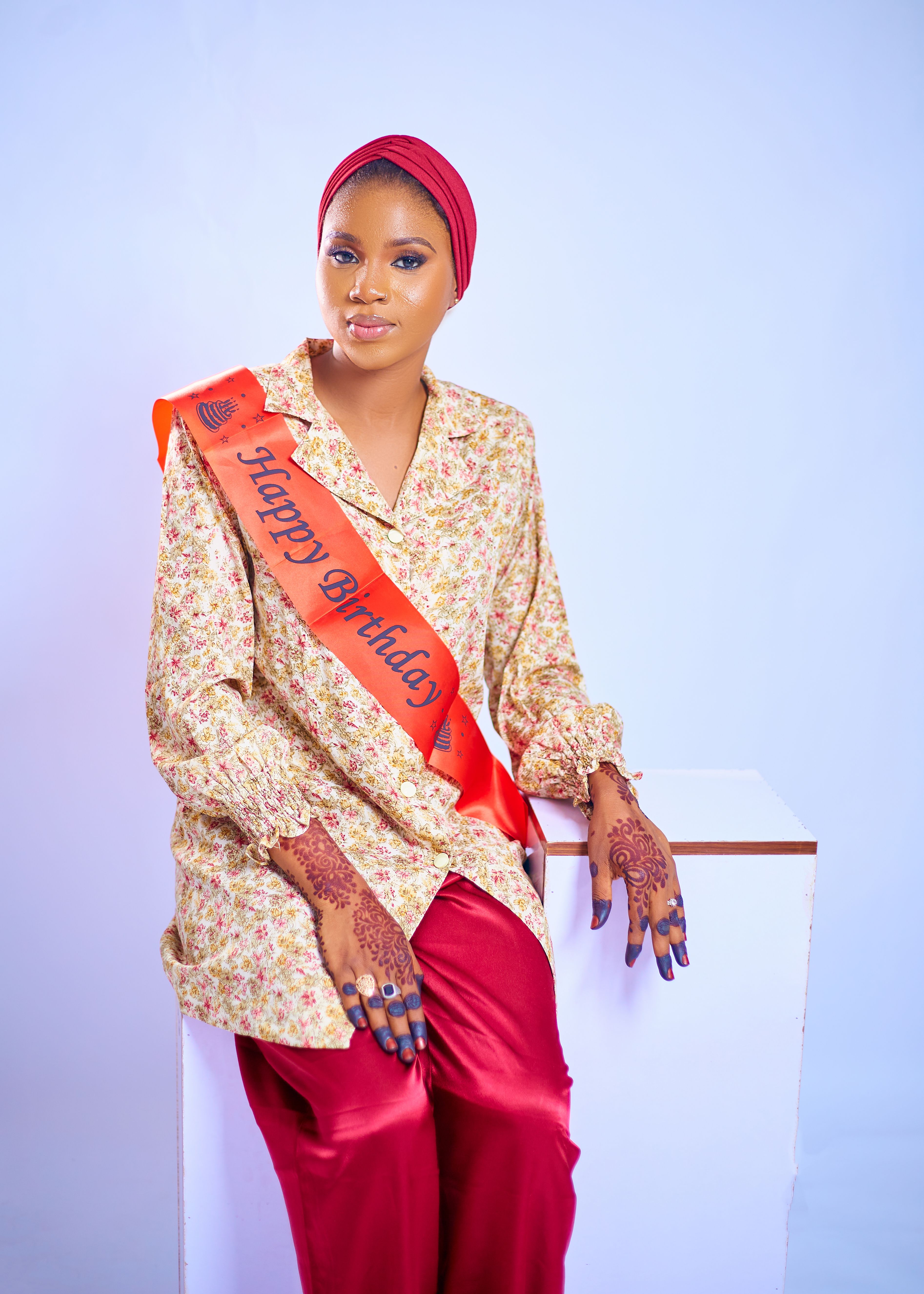 Stylish woman wearing henna and red sash celebrates her birthday indoors.