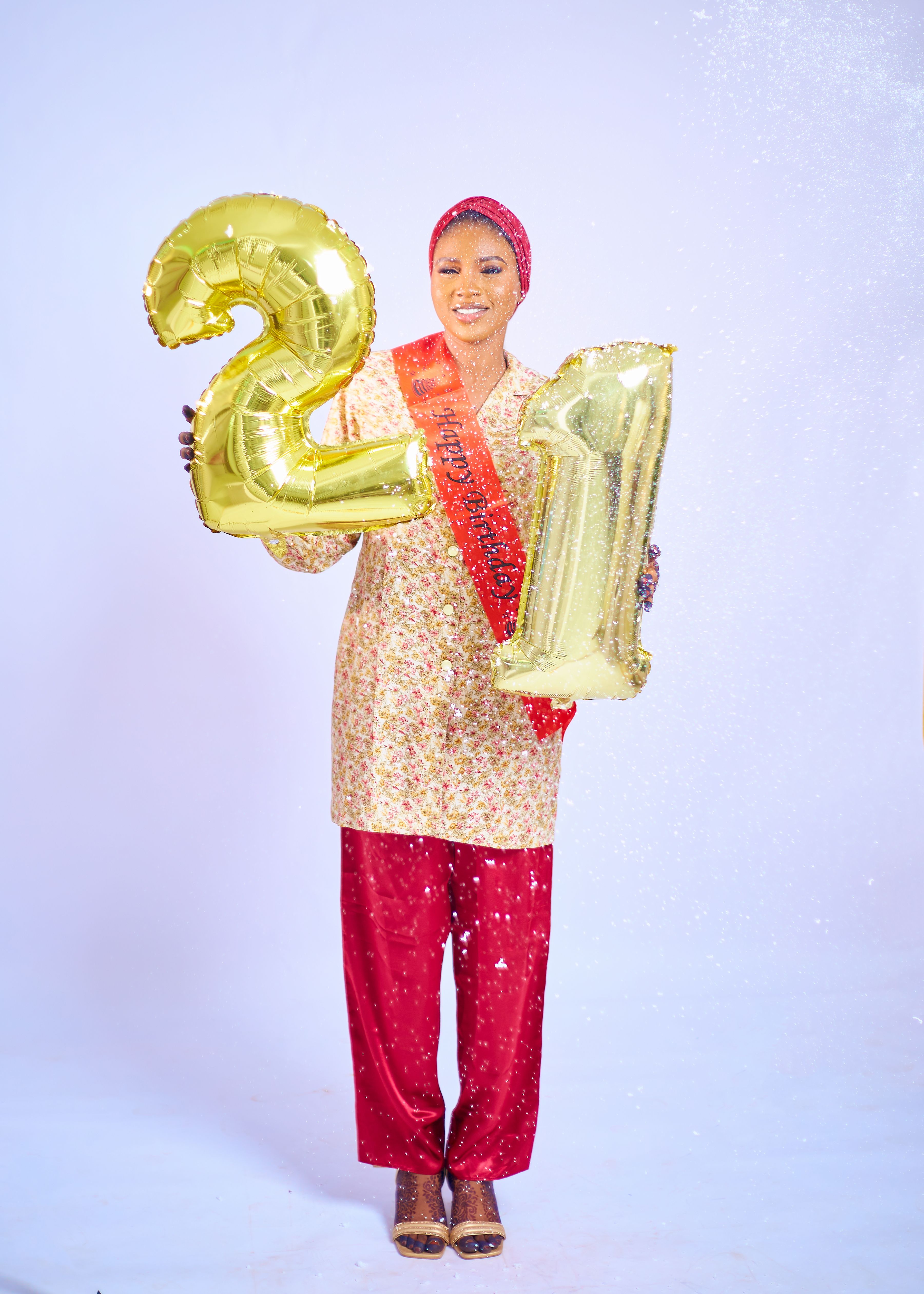 Smiling woman celebrating her 21st birthday with golden balloons, wearing vibrant attire.
