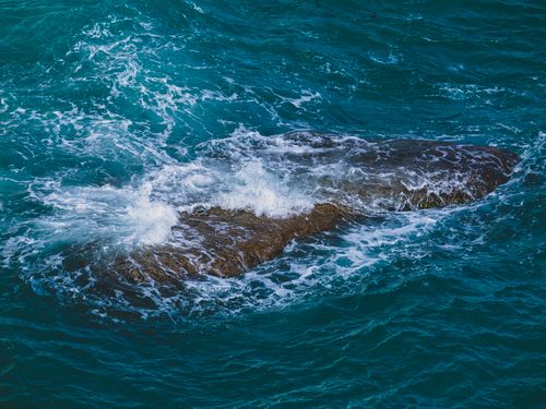 Free Aerial view of ocean waves crashing over a rocky seascape, creating dynamic water movement. Stock Photo