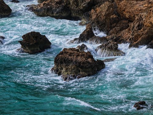 Free Capture the dynamic clash of turquoise waves on a rugged rocky coastline. Stock Photo