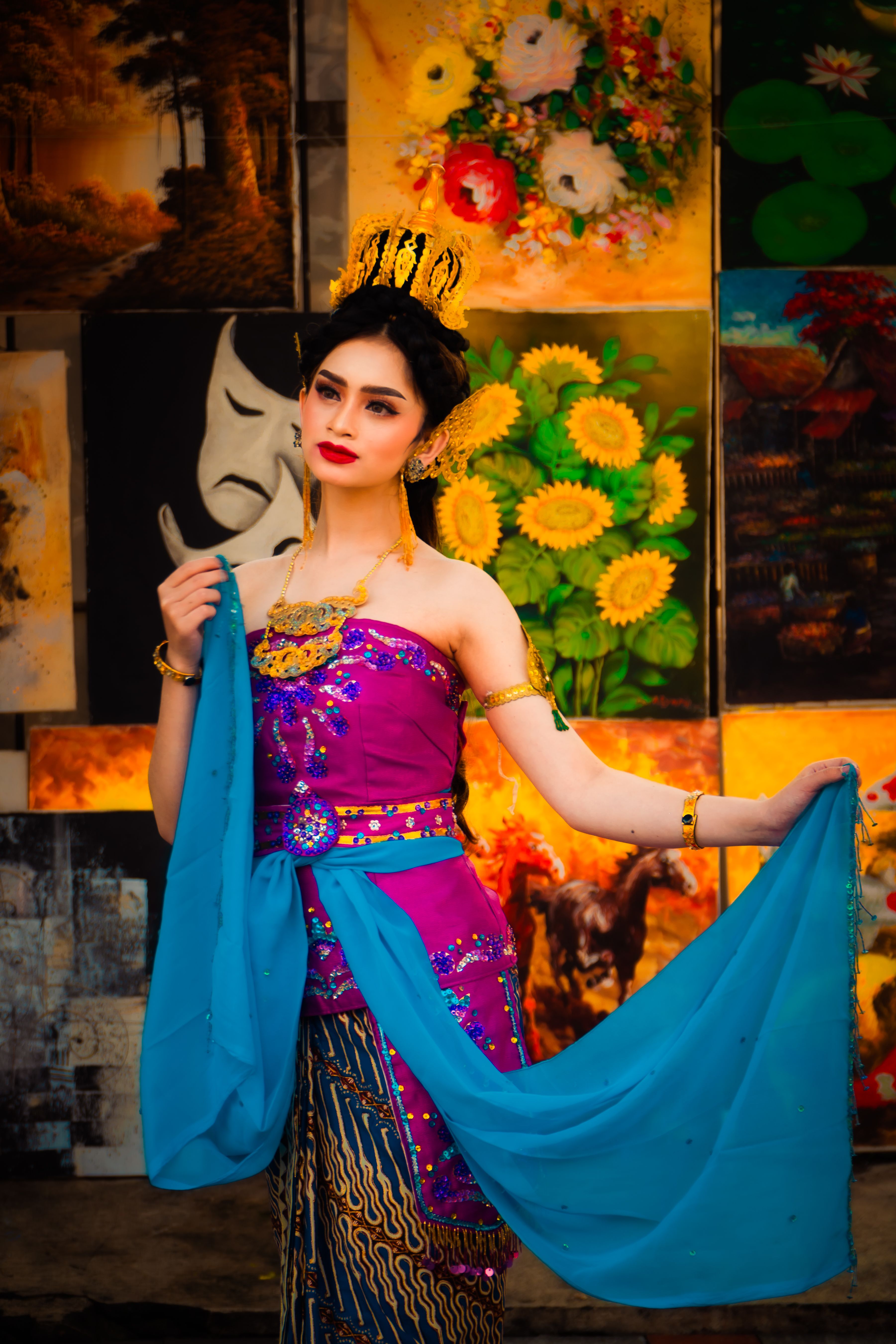 Portrait of a woman in traditional Asian attire showcasing colorful vibrant clothing in front of artistic paintings.