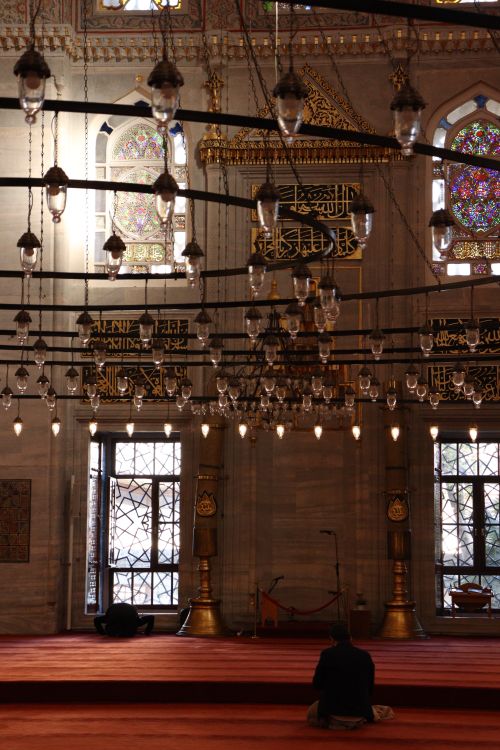 Free A peaceful interior view of a mosque with intricate stained glass and hanging lamps. Stock Photo