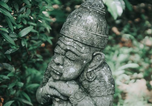 Free A serene stone statue amidst green foliage in an outdoor garden. Stock Photo
