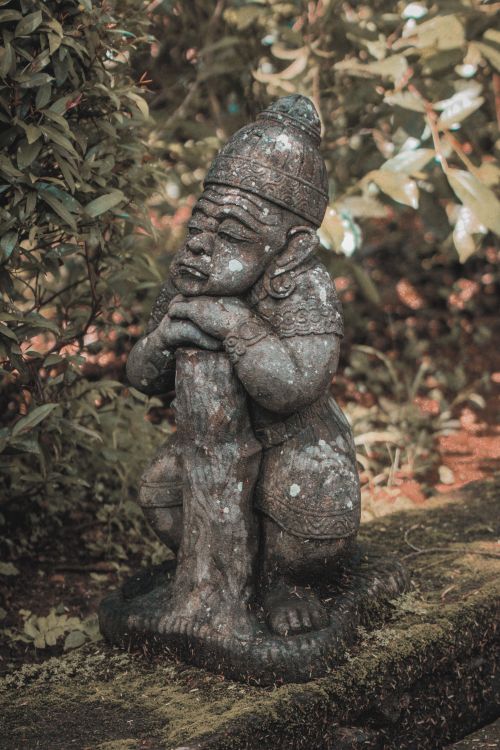 Free Close-up of an ancient stone statue with intricate details nestled in a verdant garden. Stock Photo