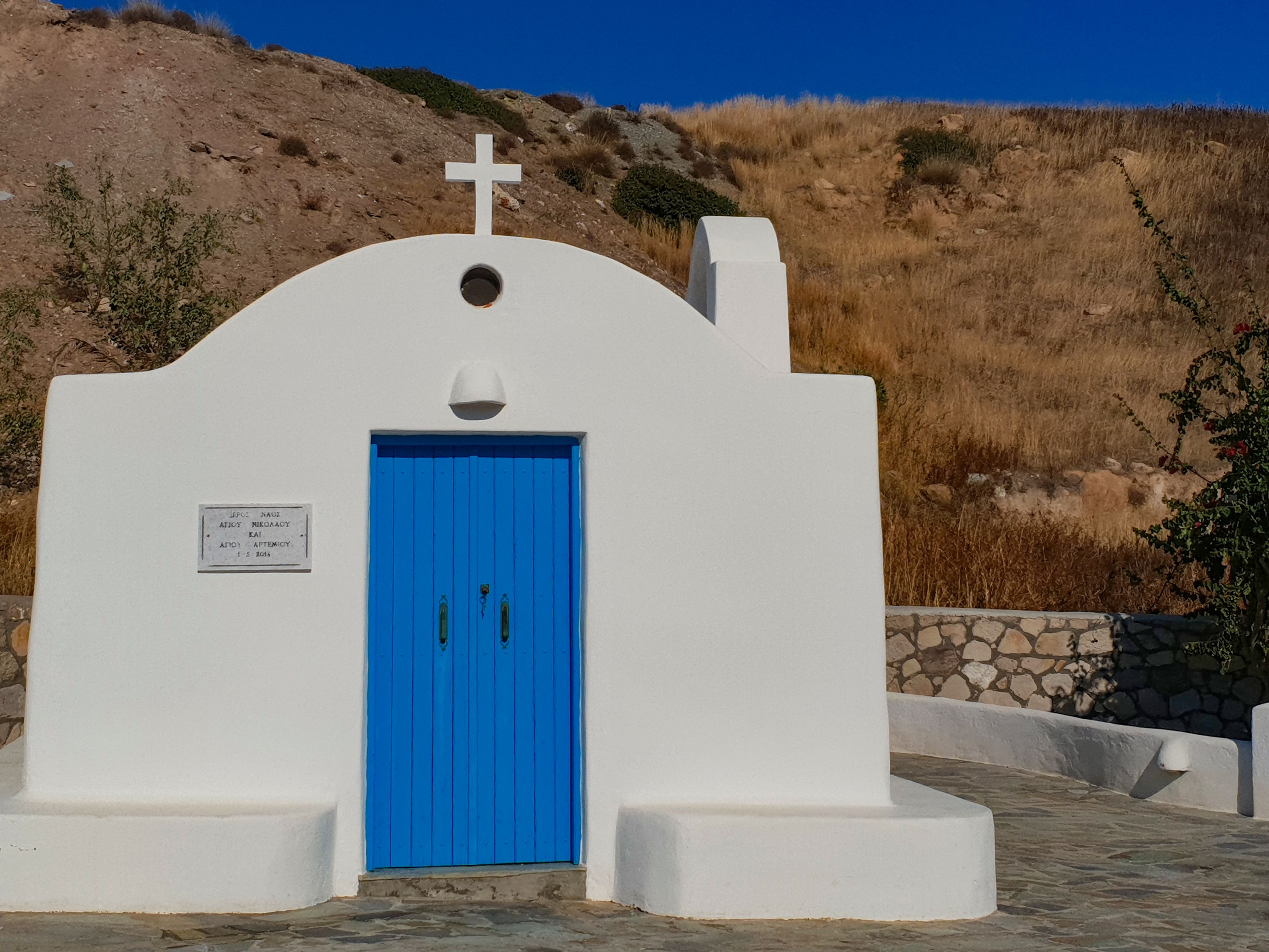 White chapel with a blue door on a rocky hillside on Anafi