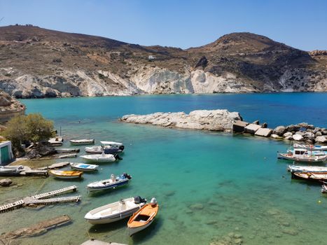 Discover the serene beauty of Milos Island's bay, featuring crystal clear waters, boats, and rocky cliffs.
