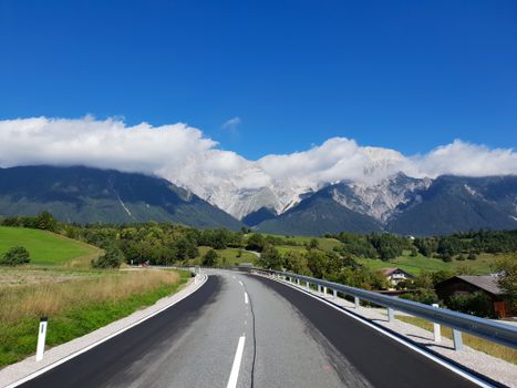 Peaceful alpine road winding through lush green hills with majestic mountain backdrop.