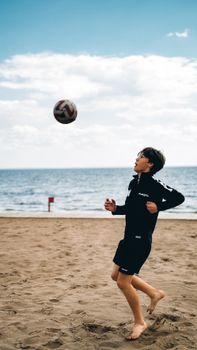 Teenage boy playing soccer on a sandy beach under a bright blue sky.