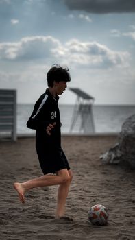 Teenager playing soccer on a sandy beach during sunset with a cloudy sky.