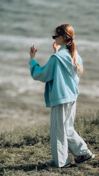 Casual young woman capturing moments by the ocean in a relaxed setting.