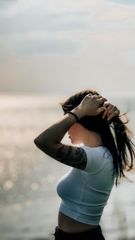 Silhouette of a woman with tattoos by the ocean during sunset, capturing a peaceful moment.
