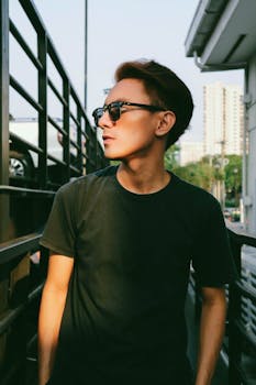 阳光明媚的城市环境中，一位戴着太阳镜的年轻人自信地摆着姿势